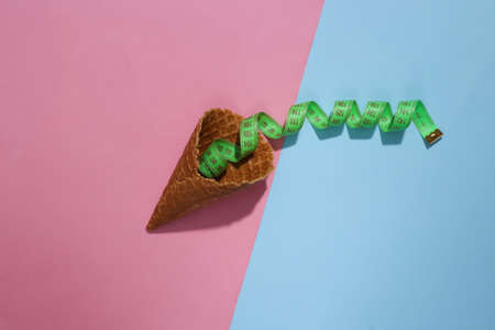Diet, weight loss concept. Ice cream waffle cone with measuring tape on pink and blue bright pastel background with deep shadow, top view. flat lay minimal compositionの写真素材