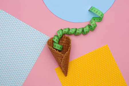 Diet, weight loss concept. Ice cream waffle cone with measuring tape on colored background, top view. flat lay minimal compositionの写真素材