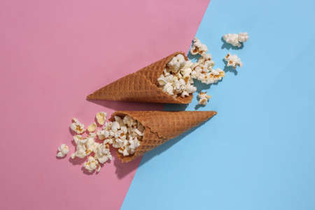 Ice cream waffle cones with popcorn on pink and blue bright pastel background with deep shadow, top view. flat lay minimal compositionの写真素材