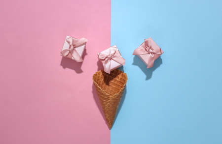 Ice cream waffle cone with gift boxes on pink and blue bright pastel background with deep shadow, top view. flat lay minimal compositionの写真素材