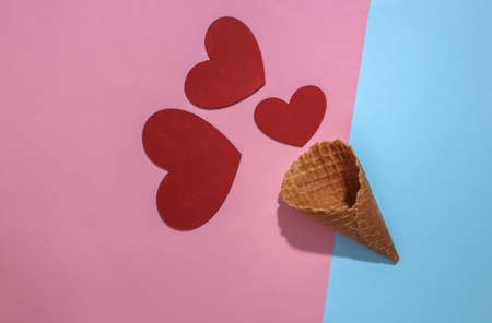 Ice cream waffle cone with red hearts on pink and blue bright pastel background with deep shadow, top view. flat lay minimal compositionの写真素材
