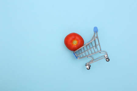 Supermarket trolley with tomato on blue background. Minimalist food flat lay. top viewの写真素材