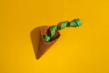 Diet, weight loss concept. Ice cream waffle cone with measuring tape on yellow background with deep shadow, top view. flat lay minimal compositionの写真素材