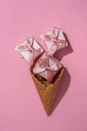 Ice cream waffle cone with gift boxes on pink bright pastel backgroundの写真素材