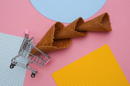 Shopping trolley with Ice cream waffle cones on creative colorful paper background, top view. flat lay minimal compositionの写真素材