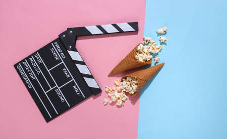 Movie clapboard, ice cream waffle cones with popcorn on pink and blue bright pastel background with...