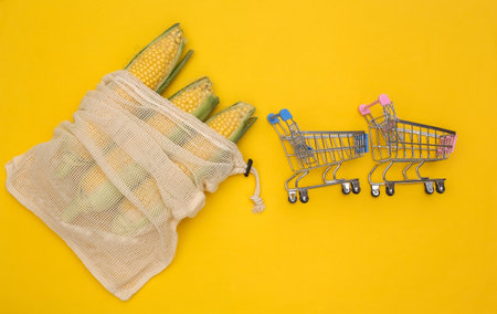 Eco cotton bag with corn swings and supermarket rolley on yellow background. top view. flat layの写真素材