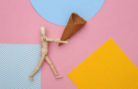 Wooden puppet holding Ice cream waffle cone on colored background. top view. flat layの写真素材
