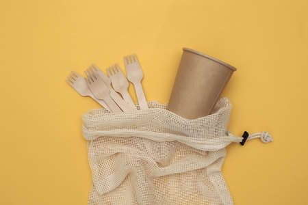 Eco cotton bag with wooden spoons and cardboard cup on yellow background. Eco friendly concept. top viewの写真素材