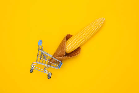 Mini supermarket trolley with swing of corn in ice cream waffle cone on yellow background. top view. Minimalism food flat layの写真素材