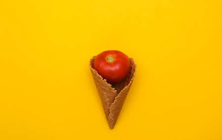 Tomato in ice cream waffle cone on yellow background. top view. Minimalist flat lay