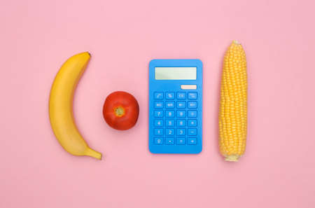 The concept of saving on food. Calculator, vegetables and fruits on a pink background. top view minimalist compositionの写真素材