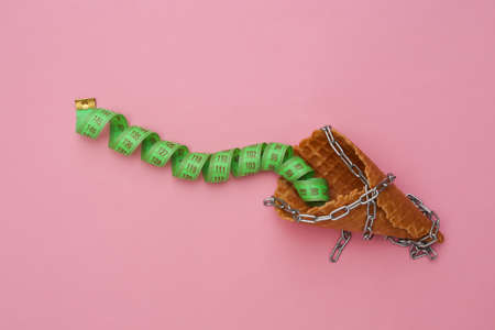 Diet, weight loss concept. Chain-wrapped Ice cream waffle cone with measuring tape on pink background, top view. flat lay minimal compositionの写真素材