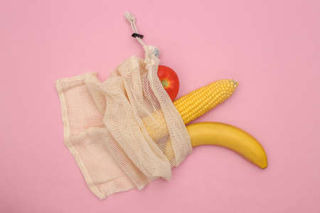 Swing of corn, tomato and banana in eco cotton bag on pink pastel background. top viewの写真素材