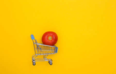 Supermarket trolley with tomato on yellow background. Minimalist food flat lay. top viewの写真素材