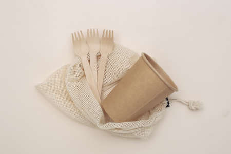 Eco cotton bag with wooden spoons and cardboard cup on beige background. Eco friendly concept. top...