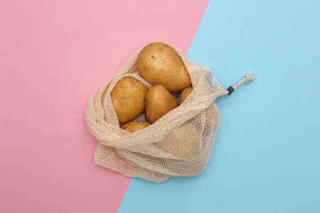 Potatoes in eco cotton bag on pink blue pastel backgroundの写真素材
