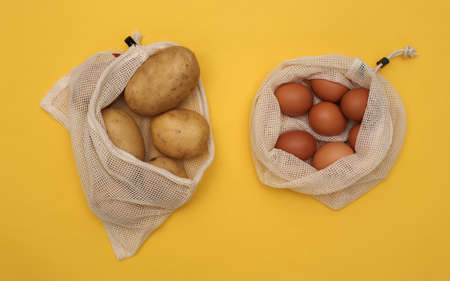 Lots of chicken eggs and potato in eco cotton bag on yellow background. top viewの写真素材