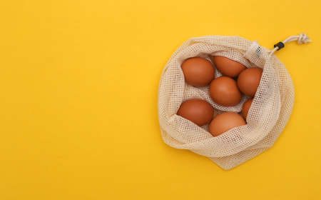 Lots of chicken eggs in eco cotton bag on yellow background. top viewの写真素材