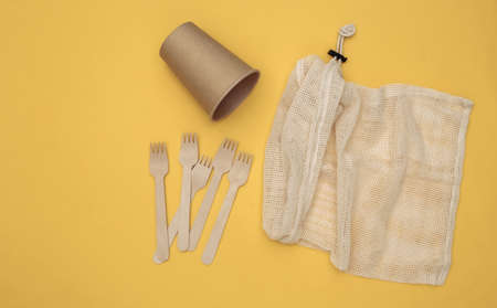 Eco cotton bag with wooden spoons and cardboard cup on yellow background. Eco friendly concept. top viewの写真素材