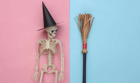 Skeleton in a witch's hat and broomstick. Blue and pink pastel background. Halloween minimalistic concept. top view. flat layの写真素材