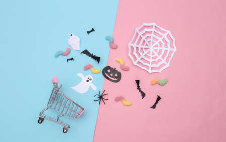 Supermarket trolley with handmade Halloween paper decor, gummy worms on pink blue pastel background. top viewの写真素材