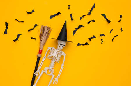 Skeleton in a witch's hat and broomstick, flying bats on yellow background. Halloween handmade decor. top view. flat layの写真素材