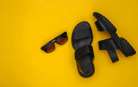 Leather black women's sandals and sunglasses on yellow background. top view. flat layの写真素材
