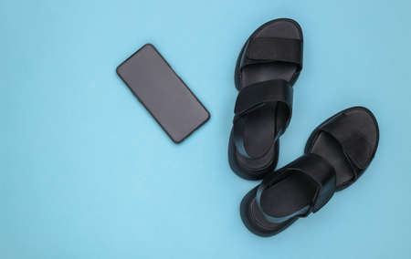 Leather black women's sandals and smartphone on blue background. top view. flat layの写真素材
