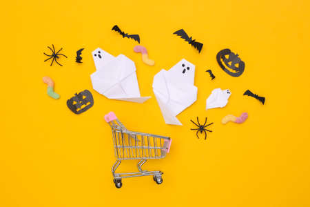 Supermarket trolley with handmade Halloween paper decor, gummy worms on yellow background. top viewの写真素材