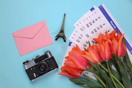 Red tulips, envelope, travel accessories and monthly calendar on blue background. top viewの写真素材
