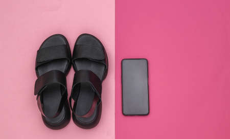 Leather black women's sandals and smartphone on pink background. top view. flat layの写真素材