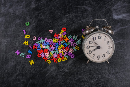 Lots of colored letters, retro alarm clock on a chalk board background. back to school. top view.の写真素材