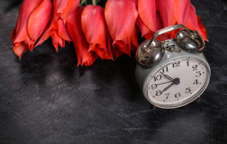 back to school. Knowledge, Teacher's Day. Bouquet of red tulips and alarm clock on chalk board.の写真素材