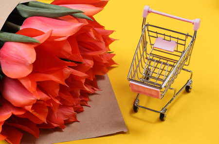 Bouquet of red tulips and supermarket trolley on yellow background.の写真素材