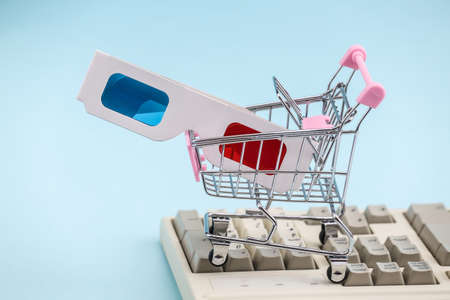 Shopping trolley with Anaglyph 3D glasses on old pc keyboard. blue background. Retro Attributes 80s