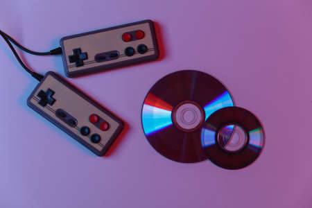 Retro gamepads and CD's in red blue gradient neon light. Gaming, video game competition. top viewの写真素材
