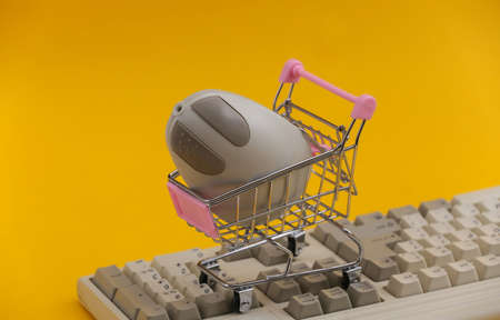Shopping trolley with retro pc mouse on old pc keyboard. yellow background. Retro Attributes 80sの写真素材