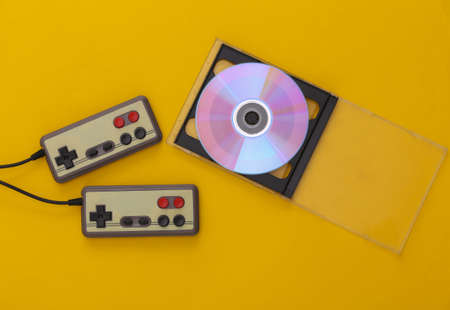 Retro gamepads, CD in box on yellow background. Gaming, video game competition. top view