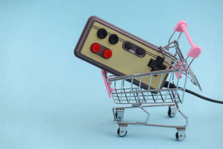 Shopping trolley with retro gamepad on blue background. Retro Attributes 80s