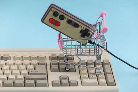 Shopping trolley with retro gamepad on old pc keyboard. blue background. Retro Attributes 80sの写真素材
