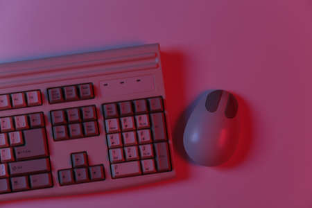 Old pc keyboard and mouse in pink blue gradient neon light. top view. flat lay