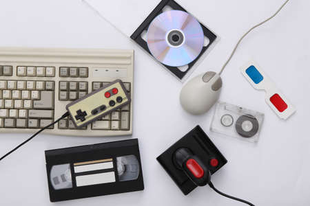 Flat lay 80s attribute composition. PC keyboard, mouse, gamepads, audio and video tapes, CDs, 3D glasses. Retro Electronics, gadgets and devices. entertainment and gaming. white background. top viewの写真素材