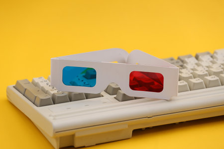 Anaglyph 3D glasses on old pc keyboard. yellow background. Retro Attributes 80s