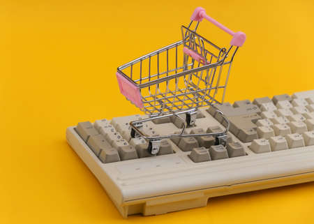 Shopping trolley on old pc keyboard. yellow background. retro online shoppingの写真素材