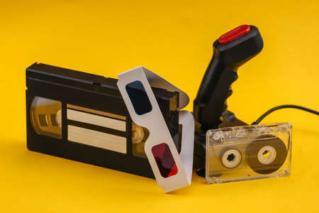 Retro joystick with 3d glasses, audio and video cassette on yellow background. Attributes 80sの写真素材