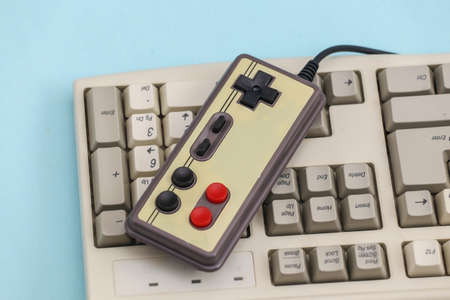 Retro gamepad on old pc keyboard. blue background. Attributes 80s, gaming