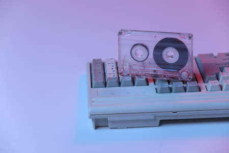 Old pc keyboard with audio cassette in pink blue gradient neon, holographic light. Retro Attributes 80sの写真素材