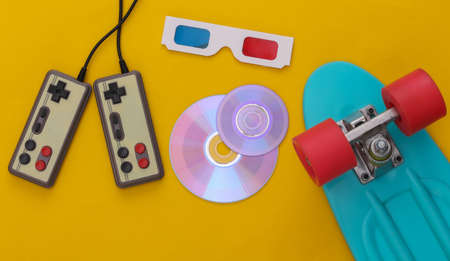 Retro entertainment, gadgets and devices. Gamepads, cruiser board, CD's, 3D glasses on yellow background. 80s. top view. flat layの写真素材