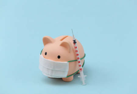 Piggy bank in medical mask with syringes on blue background. vaccination. economic disease. financial crisis. Covid-19 pandemicの写真素材